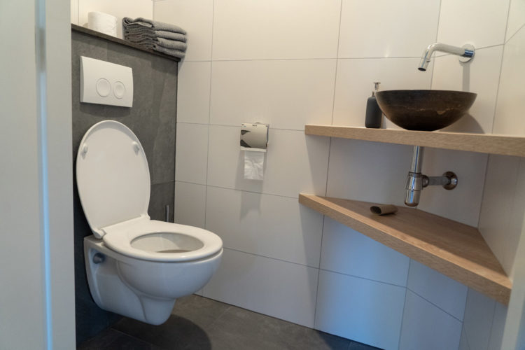 Afgewerkt toilet met getegelde wand, zwevend fonteintje en houten plank